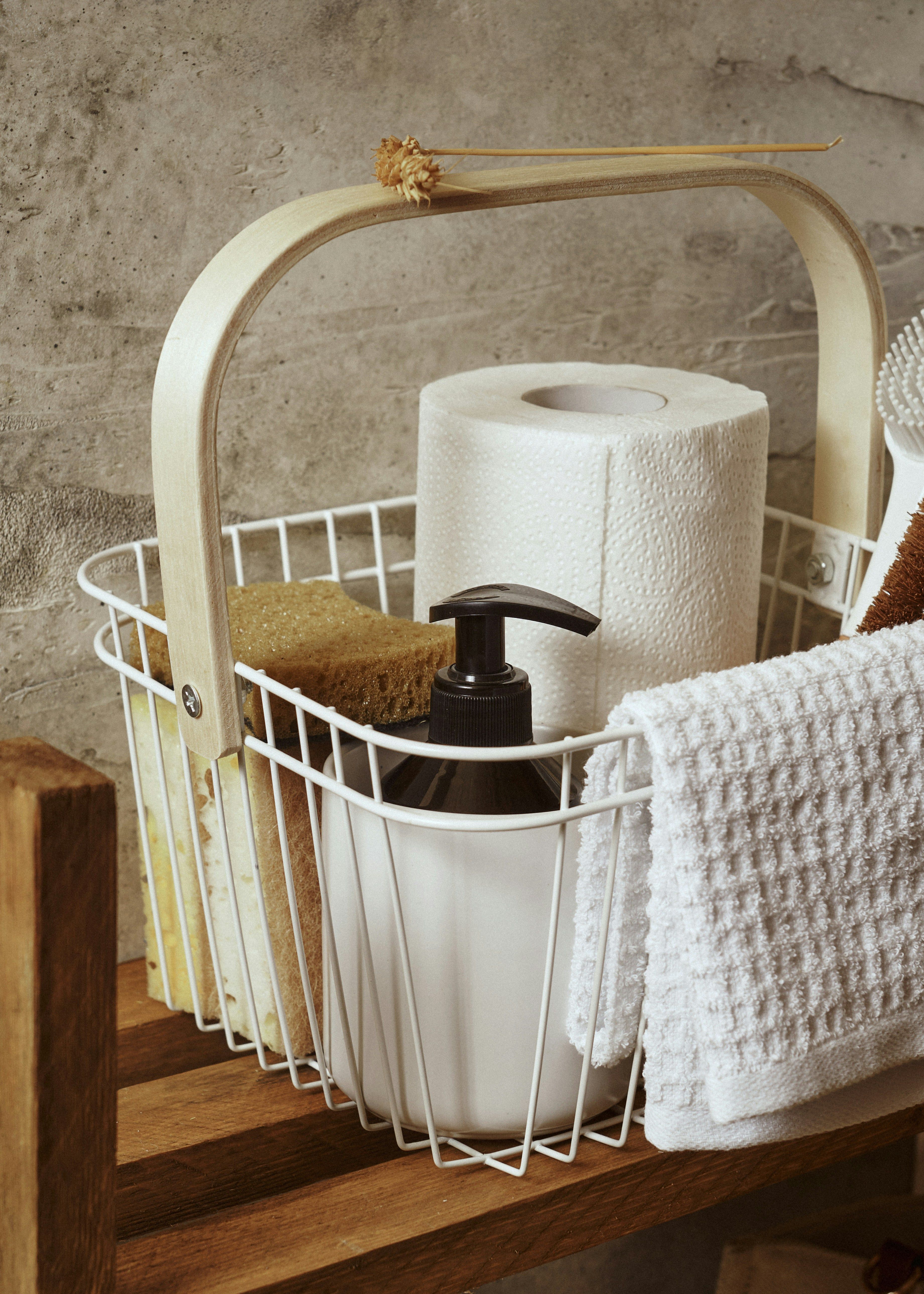 Cleaning basket with cotton cloths, sponge, soap, and a paper towel roll